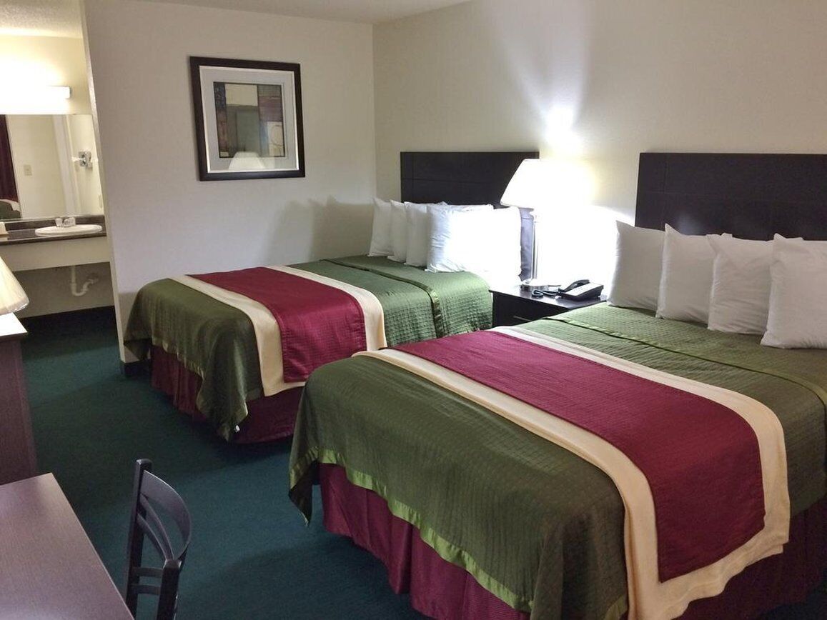 Habitación de hotel con dos camas, un escritorio, una silla, un espejo y una mesita de noche con lámpara.