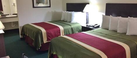 Habitación de hotel con dos camas, un escritorio, una silla, un espejo y una mesita de noche con lámpara.