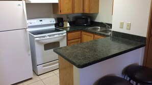 A kitchen with wooden cabinets, a white refrigerator, a stove, a microwave, and a granite countertop. - Travel Inn & Suites (Atlanta)