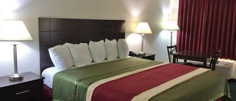 A hotel room with a large bed, two bedside tables with lamps, a desk with a chair, and a window with curtains.