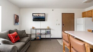 A compact living space with a sofa, a coffee table, a kitchen area with a refrigerator, and a door. - Blocks from Yellowstone Park Bison at Buffalo Jump (West Yellowstone)