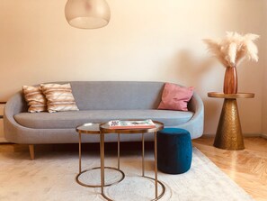 A modern living room with a grey sofa, two side tables, a blue ottoman, and a decorative vase with pampas grass.