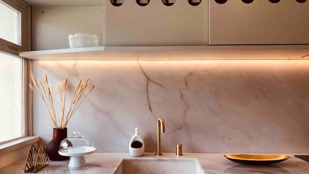 Una cocina moderna con encimera de mármol, grifo dorado y diseño minimalista.