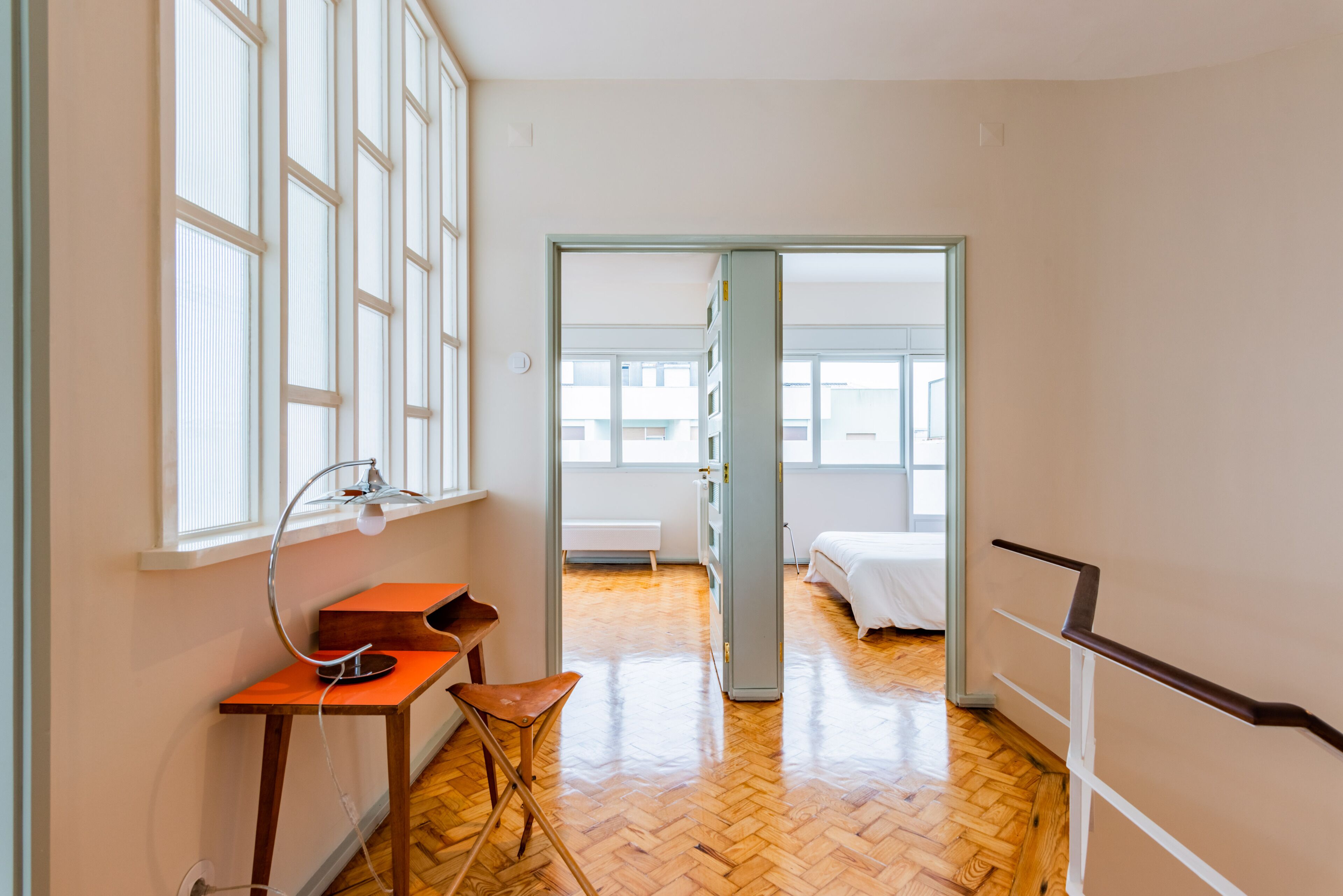 Ein Zimmer mit Holzboden, Schreibtisch mit Lampe, Stuhl und Bett.
