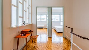 Una habitación con piso de madera, un escritorio con lámpara, una silla y una cama.