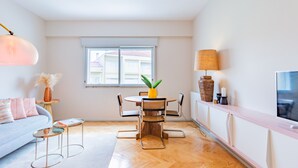 Una sala moderna con un sofá, una mesa de comedor con sillas, una lámpara y un televisor sobre un mueble.
