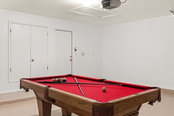 Una mesa de billar en una habitación con paredes y puertas blancas.