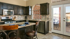 A kitchen with dark cabinets, a stainless steel stove, a microwave, and a coffee maker. There is a large island with a glass top and stools. A dishwasher is visible to the right. - Hot tub with city views 
     -NO PARTIES ALLOWED- (Albuquerque)
