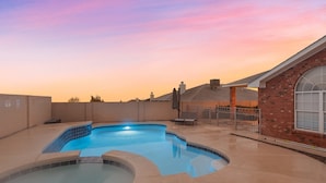 A swimming pool with a curved design, surrounded by a brick building and a metal fence. - Hot tub with city views 
     -NO PARTIES ALLOWED- (Albuquerque)