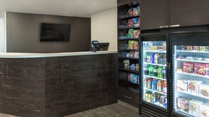 A reception area with a dark wood reception desk, a flat-screen TV mounted on the wall, and a self-service beverage dispenser stocked with various drinks. - My Place Hotel - Midland (Midland)
