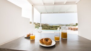 Mesa de desayuno con pasteles, vasos de jugo de naranja y una jarrón de té, con vista a un paisaje pintoresco.