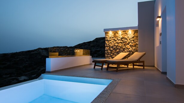 Un área de piscina moderna al aire libre con una pared de piedra y sillones de descanso.