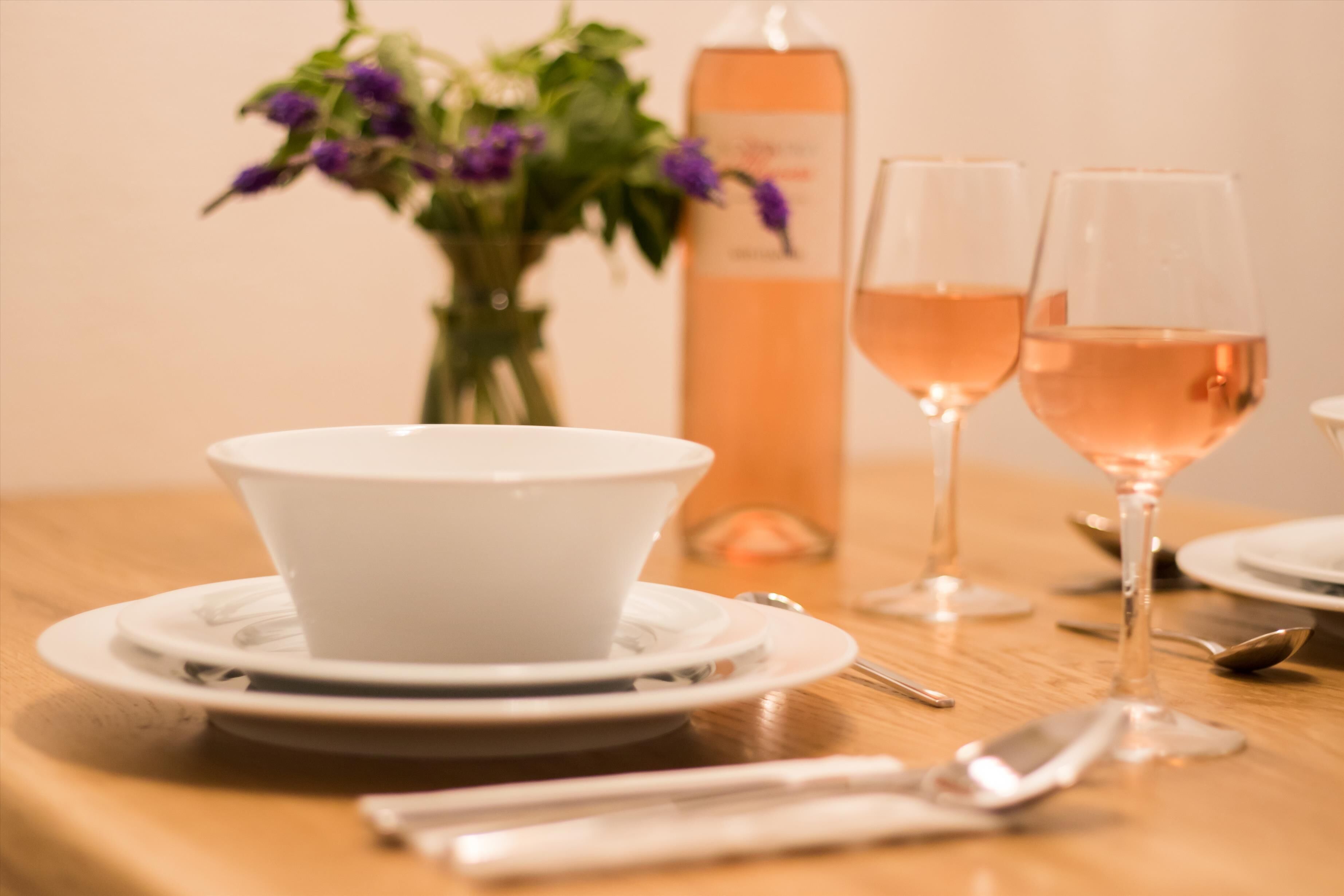 Une table à manger avec un saladier blanc, deux verres à vin et une bouteille de vin.