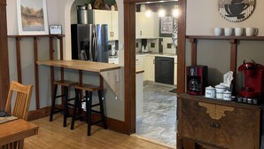 A kitchen with wooden cabinets, a wooden dining table with chairs, a refrigerator, and a coffee station with a coffee machine and cups. - Centrally located for all your activities! (Colville)