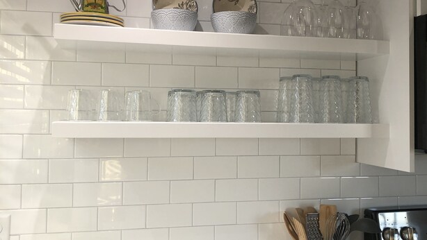A kitchen with white tiled walls, shelves holding glassware and plates, a wooden bowl, and a spice rack. - Wonderful Mid Island Gem (Nantucket)