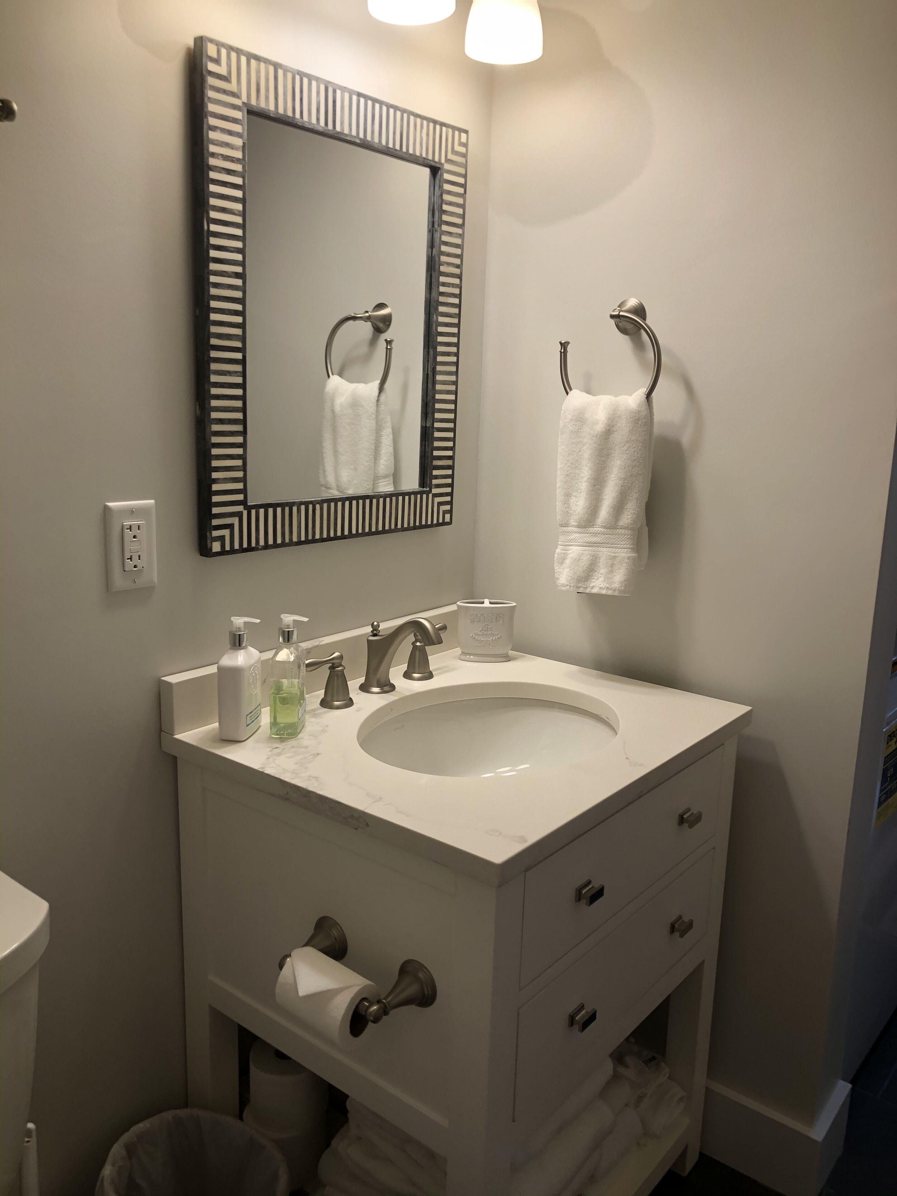 A bathroom with a white sink, a mirror with a black frame, a towel rack, and a toilet.