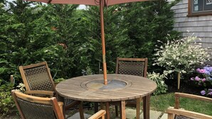 A round wooden table with four wicker chairs, an overhead umbrella, and a stone-paved patio. - Wonderful Mid Island Gem (Nantucket)