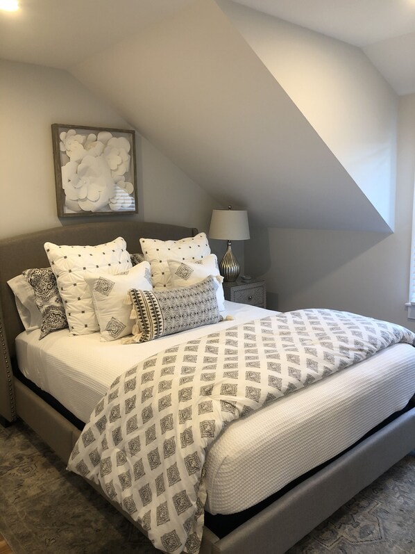 A bedroom with a bed, pillows, a bedside table, a lamp, and a wall art piece. - Wonderful Mid Island Gem (Nantucket)