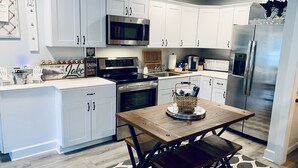 A modern kitchen with white cabinets, stainless steel appliances, and a wooden dining table. - Dreamlike Lakefront Cabin on Lake Sutherland (Port Angeles)