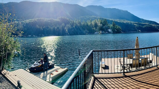 A wooden deck with outdoor seating, overlooking a calm lake with mountains in the background. - Dreamlike Lakefront Cabin on Lake Sutherland (Port Angeles)