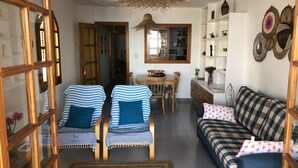 Un salon avec deux fauteuils à rayures, un canapé, une table à manger et, au fond, une cuisine.