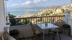 Un balcon avec une table et des chaises, offrant une vue sur un paysage urbain côtier avec une plage et des montagnes.