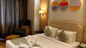 Una habitación de hotel con cama, una silla, un escritorio, una lámpara y un ventilador de techo.