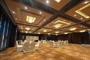 A banquet hall with round tables and white chairs, a stage, and a patterned carpet. - Comfort Hotel Vista (Lucknow)