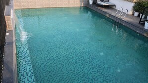Una piscina con agua azul cristalina, borde de azulejos y una escalera a la derecha.