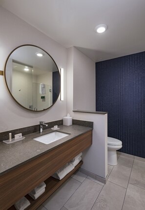 Un baño moderno con un espejo redondo, dos lavamanos, un inodoro y un perchero para toallas.