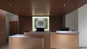 A reception area with a wooden reception desk, a seating area, and a decorative wall piece. - Fairfield Inn & Suites by Marriott Oskaloosa (Oskaloosa)