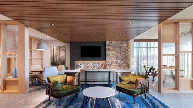 A modern living room with a round coffee table, two sofas, a TV, and a stone accent wall. - Fairfield Inn & Suites by Marriott Oskaloosa (Oskaloosa)