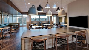 A modern restaurant with a central bar area, multiple seating options including booths and tables, and hanging pendant lights. - Fairfield Inn & Suites by Marriott Oskaloosa (Oskaloosa)