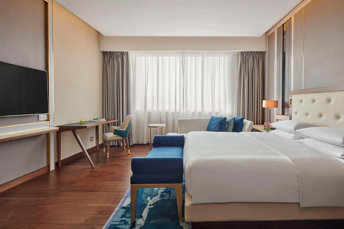 A hotel room with a bed, a desk, a TV, and a window with curtains.