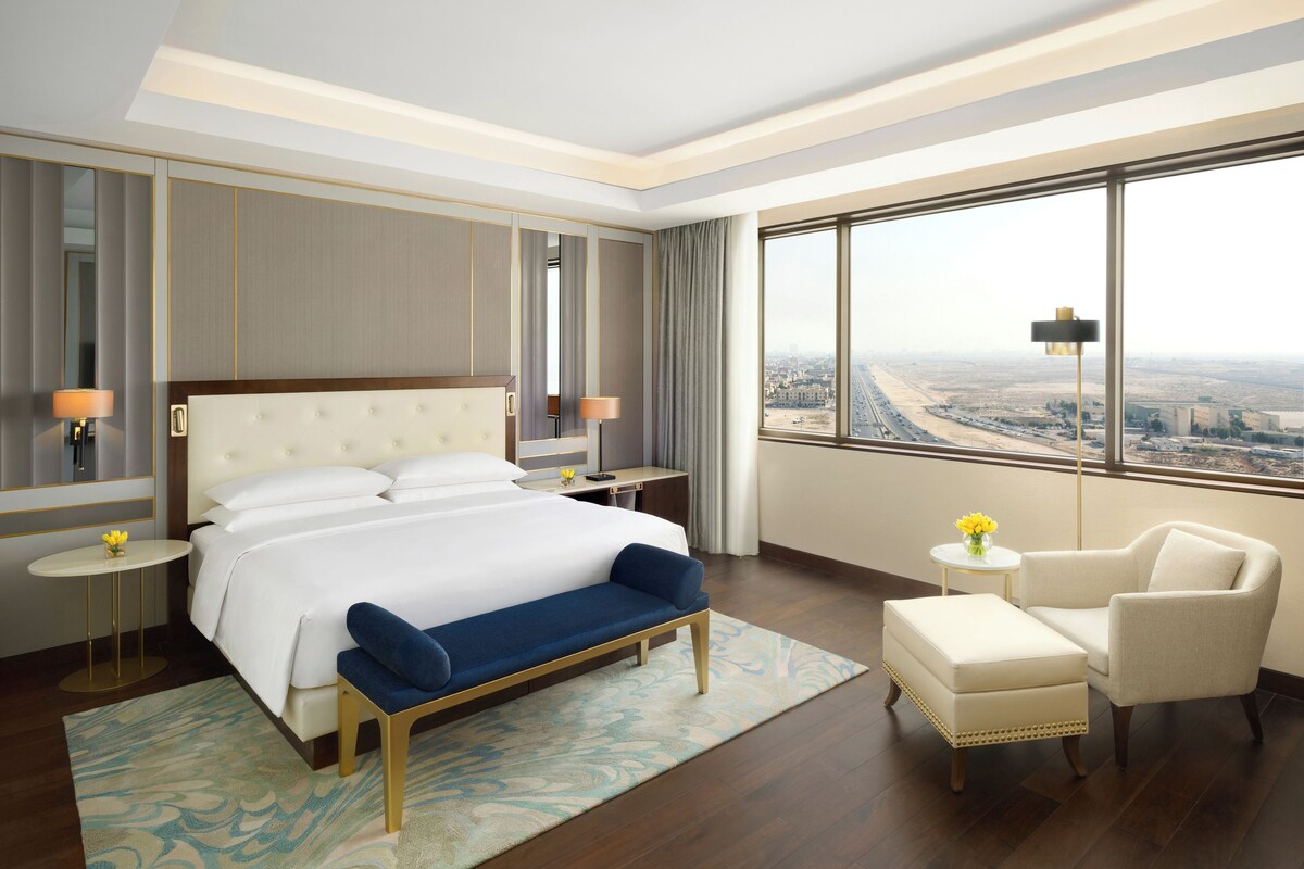Hotelkamer met een groot bed, een bank, een stoel, een klein tafeltje en uitzicht op een stadsgezicht.