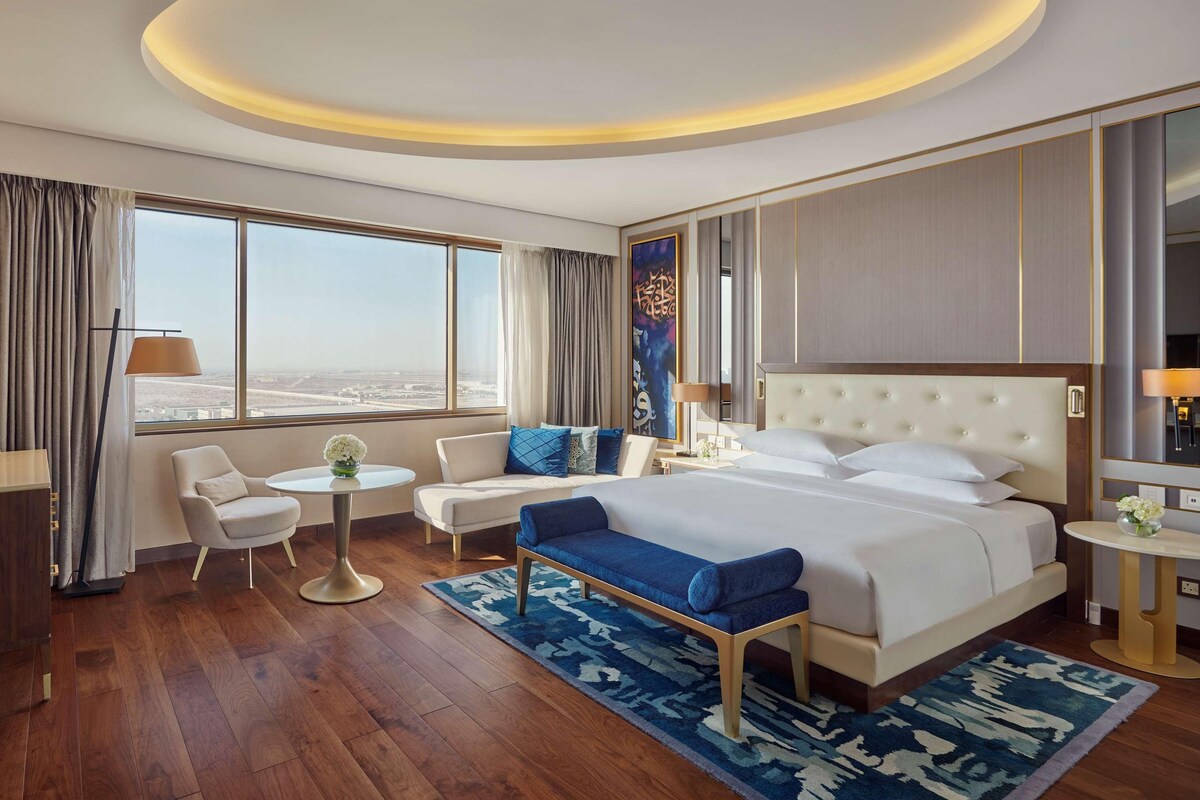 A hotel room with a large bed, a sofa, a desk, and a TV.