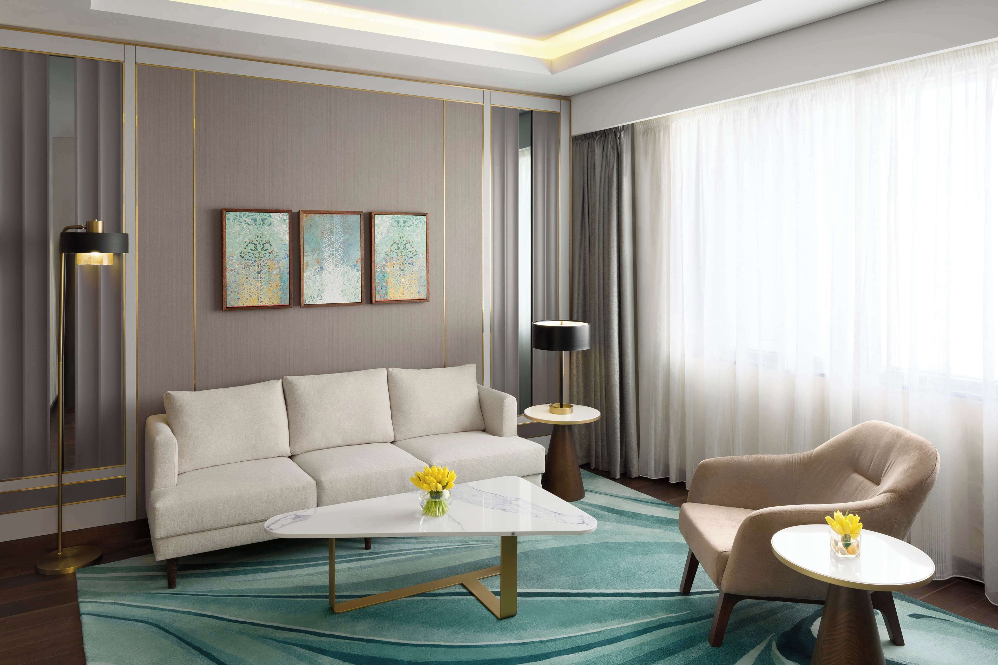 Una habitación de hotel moderna con un sofá, dos sillones, una mesa de centro y una lámpara.