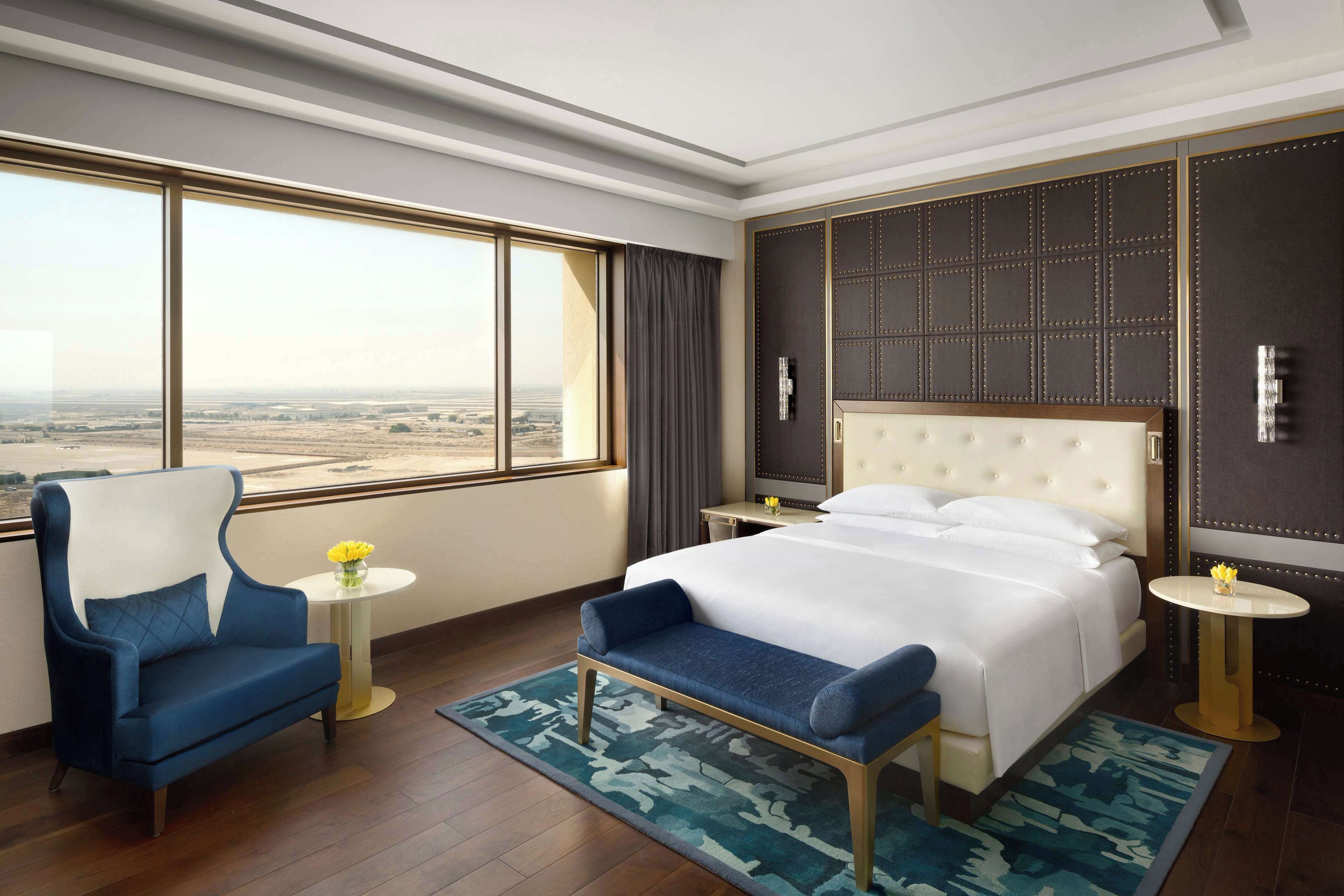 A hotel room with a large bed, a sofa, a small table, and a view of the landscape.
