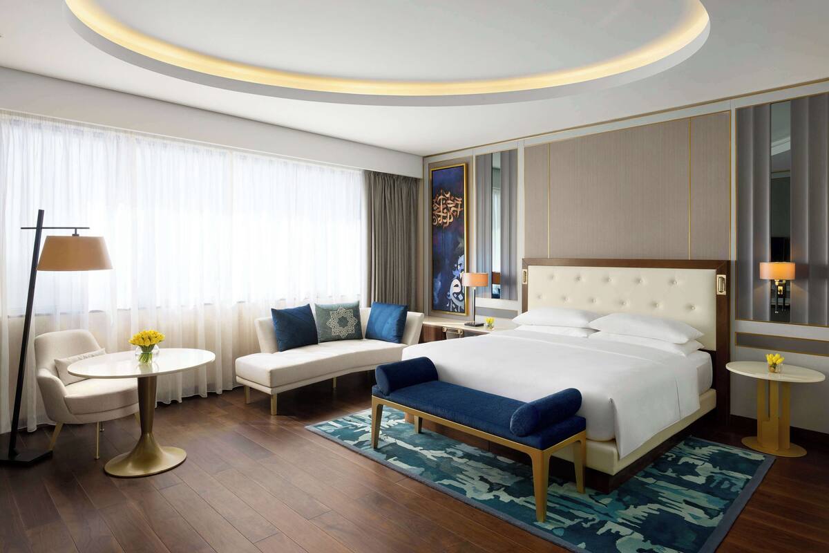A modern hotel room with a large bed, a sofa, a small table, and a desk.