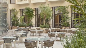 An outdoor cafe area with multiple tables and chairs, surrounded by potted plants and trees. - Grand Hyatt Alkhobar Hotel and Residences (Al Khobar)