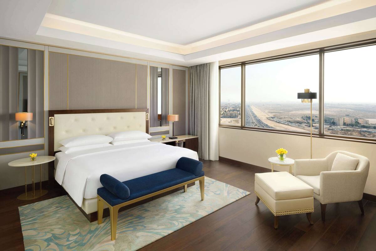A hotel room with a large bed, a sitting area, and a view of a cityscape.