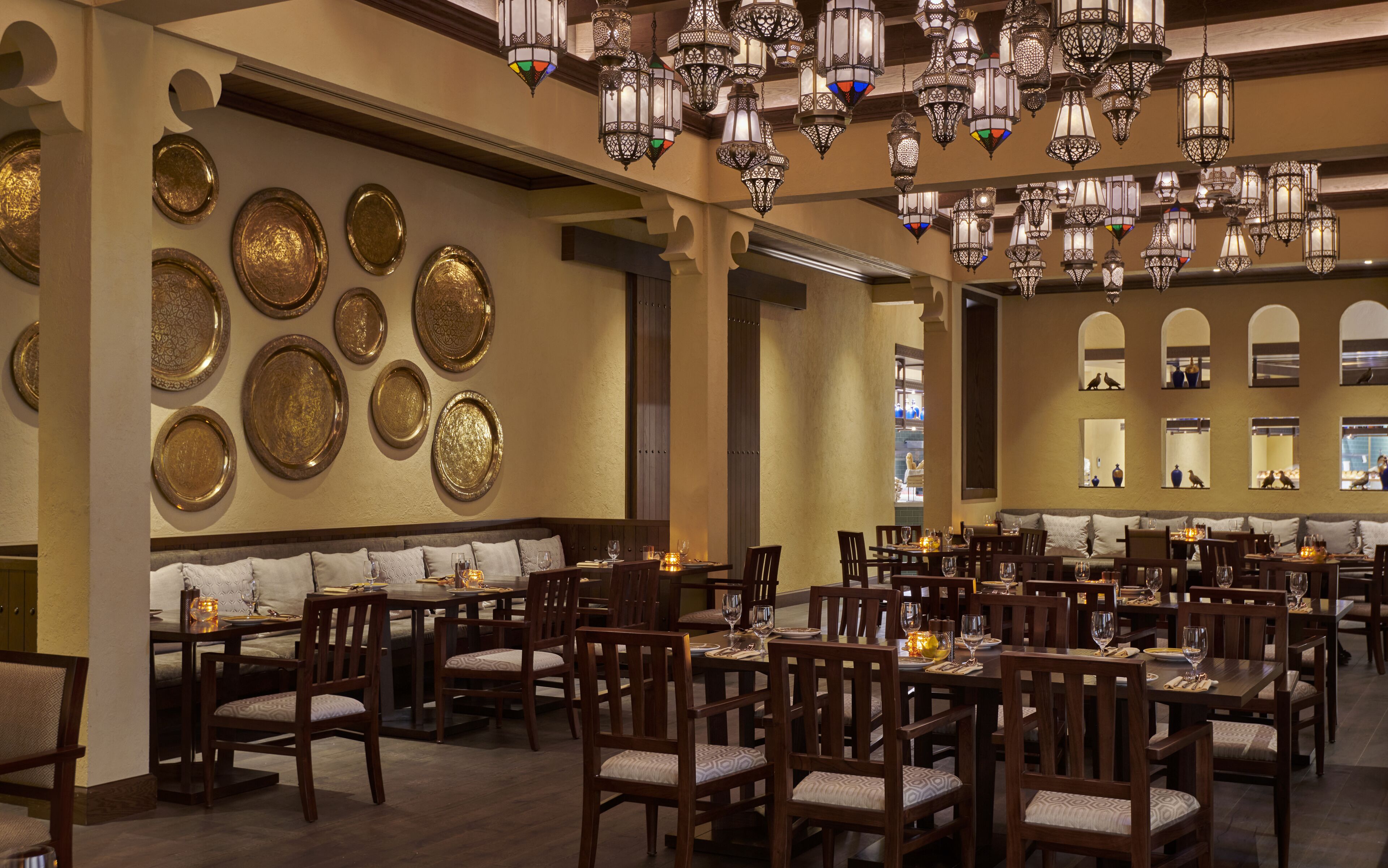 A restaurant with multiple dining tables and chairs, ornate wall decorations, and hanging lanterns.