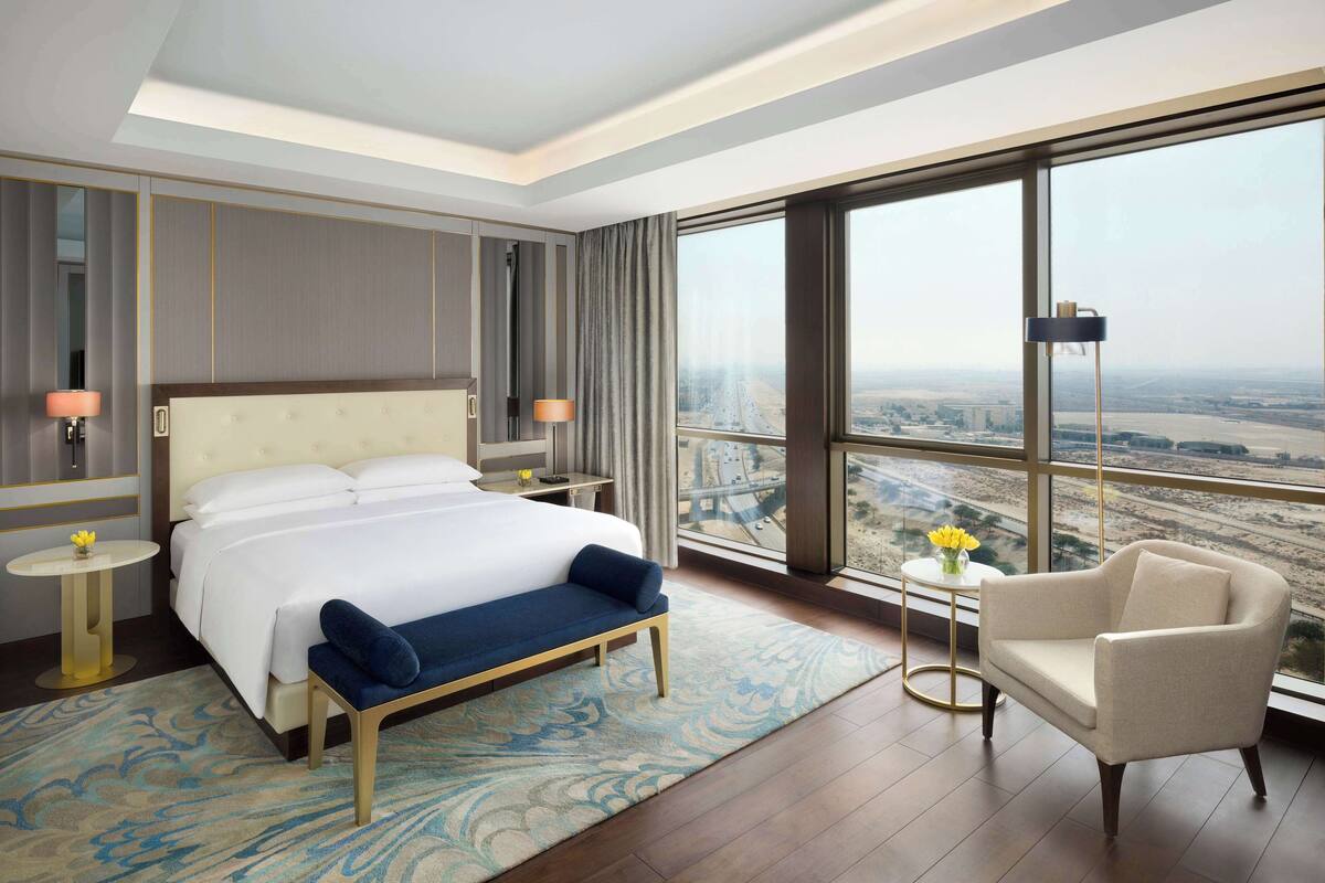 A modern hotel room with a large bed, a sitting area, and a view of a cityscape.