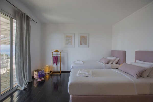 Habitación de hotel con dos camas, una ventana con cortinas, una mesita con lámpara y un perchero con toallas.