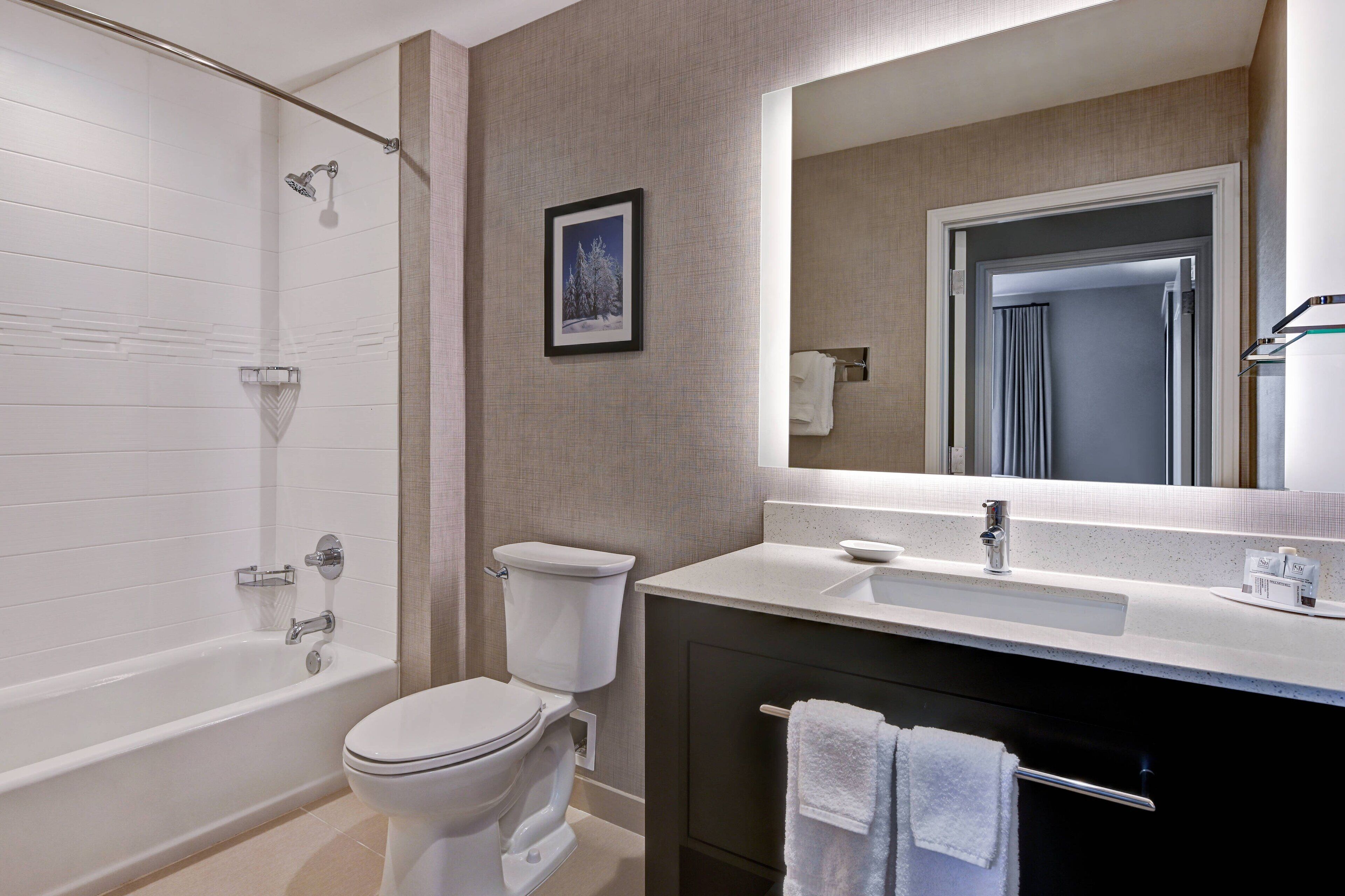 A modern bathroom with a bathtub, toilet, sink, and a large mirror.