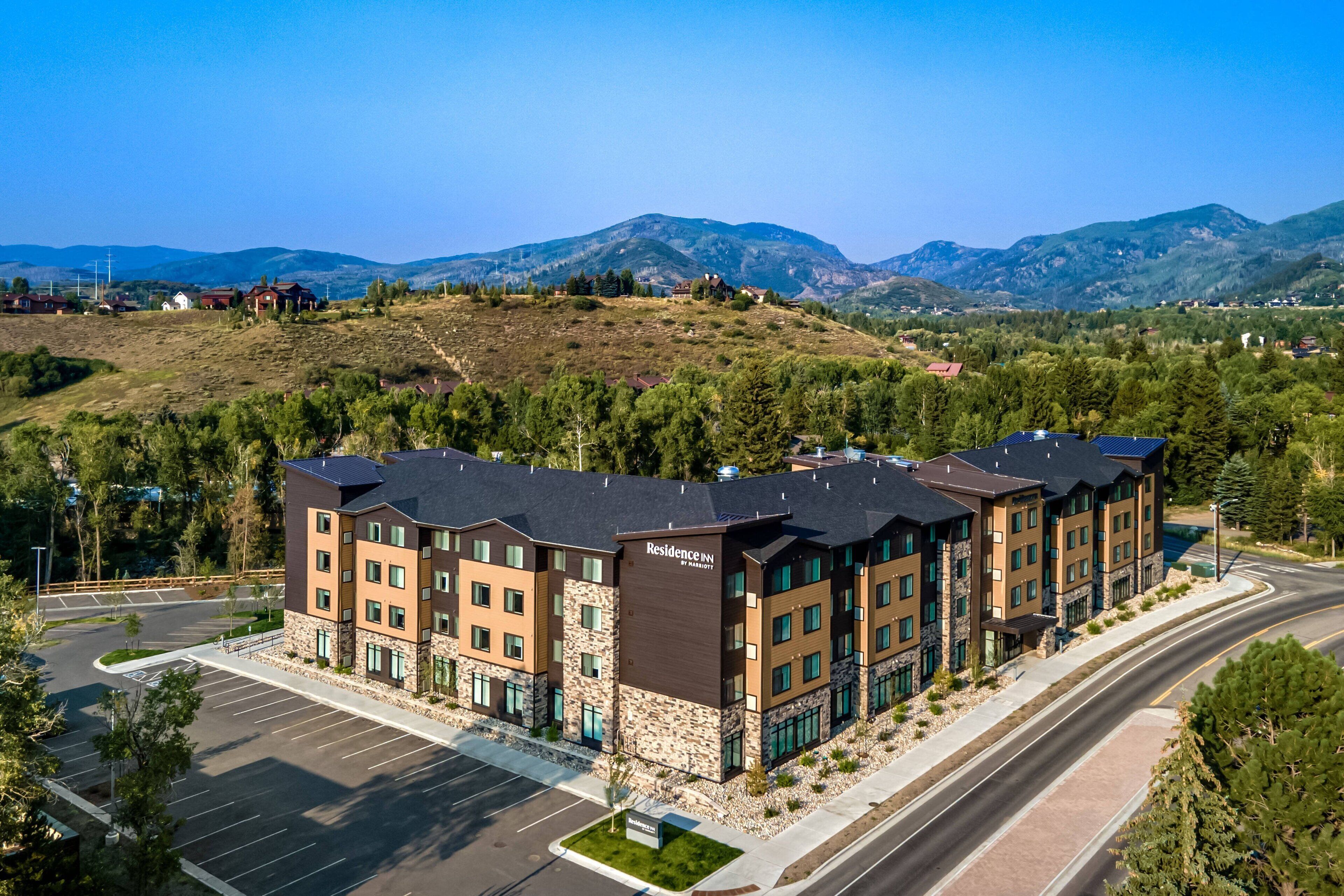A multi-story hotel with a stone facade, located in a hilly area with a parking lot and a road in the foreground.