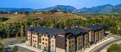 A multi-story hotel with a stone facade, located in a hilly area with a parking lot and a road in the foreground.