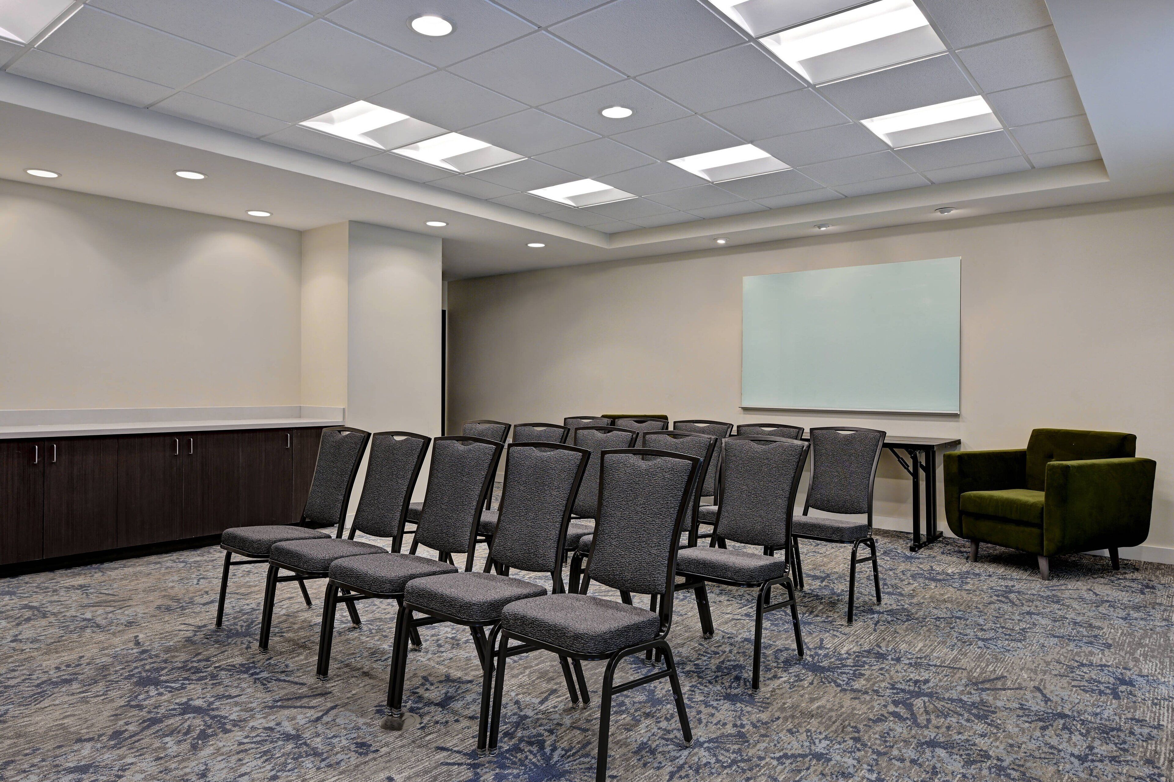 A conference room with rows of chairs, a projector screen, and a carpeted floor.