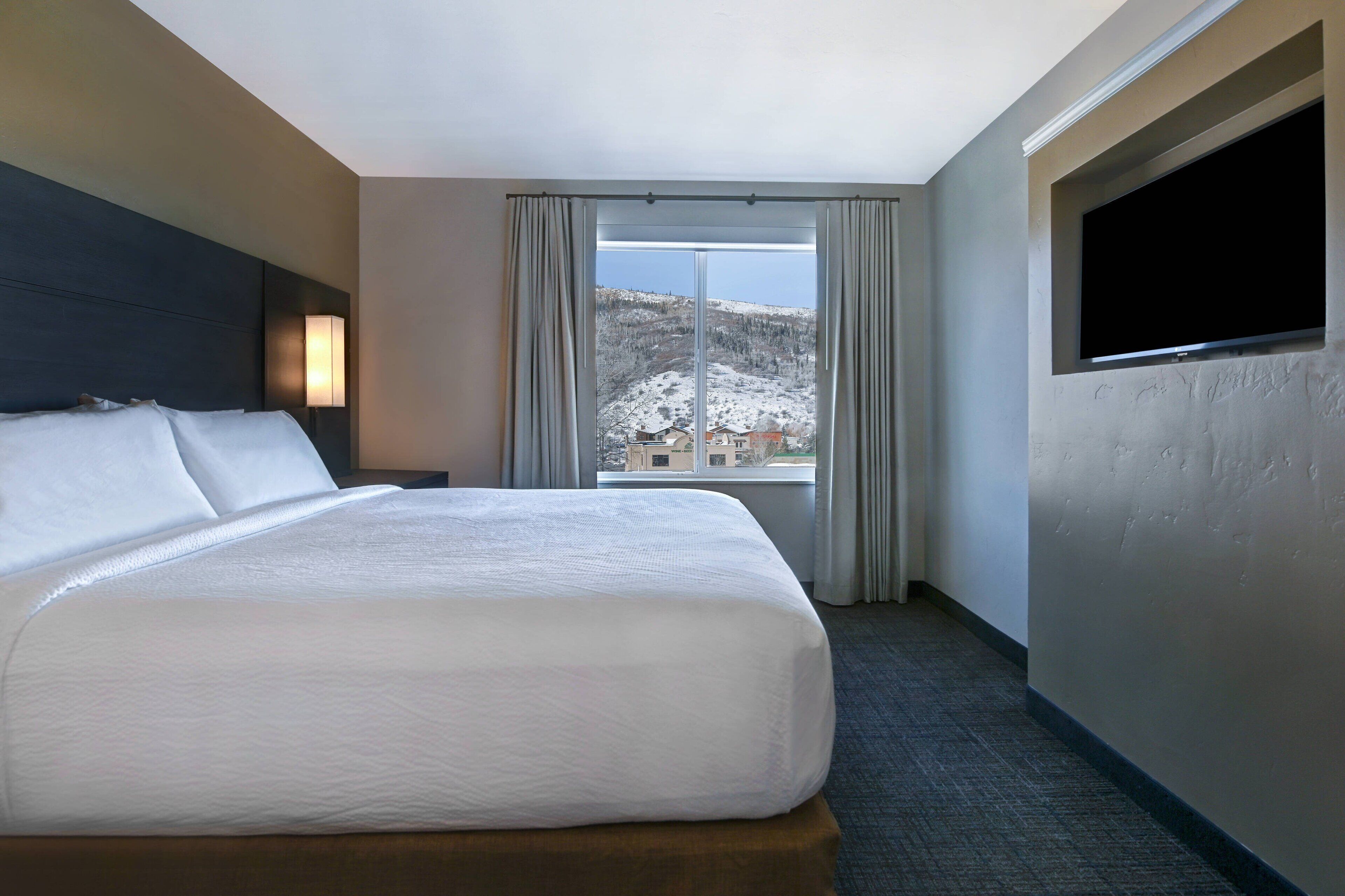 Ein Hotelzimmer mit einem großen Bett, einem flachbildfernseher an der Wand und einem Fenster mit Vorhängen.