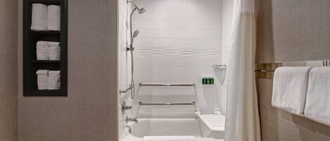 A modern bathroom with a bathtub, shower, and toilet. There are towels on the wall and a shelf with toiletries.